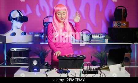 Artist with pink hair dancing and having fun in nightclub, mixing eletronic sound with techno using professional mixer. Dj performer playing remix using audio equipment, performing at musical event Stock Photo