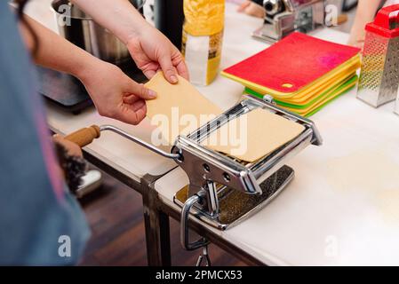Close-up of a woman hands preparing dough for pasta using rolling machine, in the kitchen Stock Photo