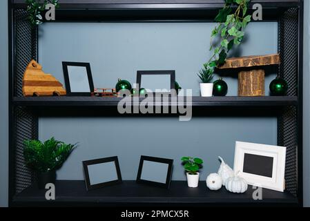 Wooden shelf painted black with blank photo frames and decorations against greyish blue wall background Stock Photo