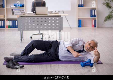 Old male employee doing sport exercises during break Stock Photo