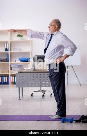 Old male employee doing sport exercises during break Stock Photo