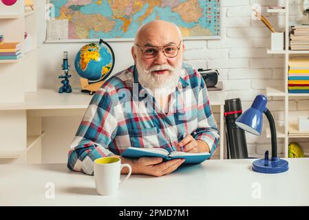 Portrait of senior teacher sitting at desk in classroom. Teaching in university. University education. Stock Photo