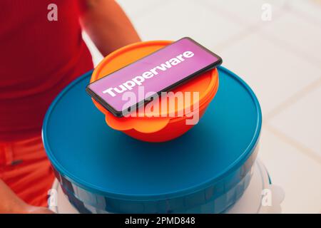 April 12, 2023: April 12, 2023, Brazil. In this photo illustration, a person carries various plastic products (containers) and a smartphone shows the Tupperware logo (Credit Image: © Rafapress/SOPA Images via ZUMA Press Wire) EDITORIAL USAGE ONLY! Not for Commercial USAGE! Stock Photo
