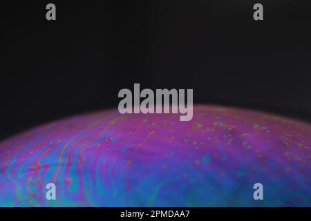 Macro of an iridescent soap bubble film forming psychedelic patterns on a black background – abstract color texture. Stock Photo