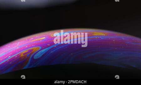 Macro of an iridescent soap bubble film forming psychedelic patterns on a black background – abstract color texture. Stock Photo
