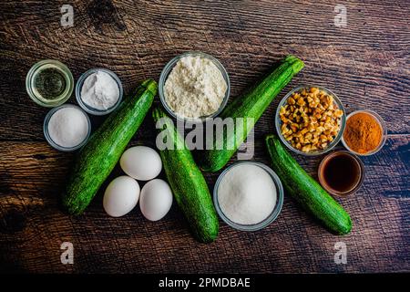 Zucchini Bread Ingredients on a Wood Table Background: Fresh zucchini, flour, walnuts, and other dessert bread ingredients Stock Photo