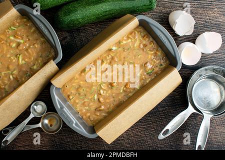 Loaf Pans Filled with Zucchini Bread Batter on a Wood Table: Nonstick bread loaf pans lined with parchment paper and filled with unbaked batter Stock Photo