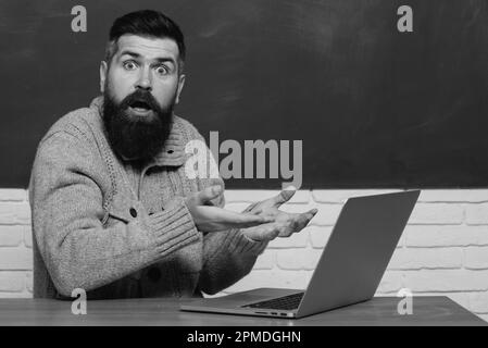 Science and education concept. Knowledge day. Student working on laptop in college. Young teacher near chalkboard in school classroom. Chalkboard for Stock Photo