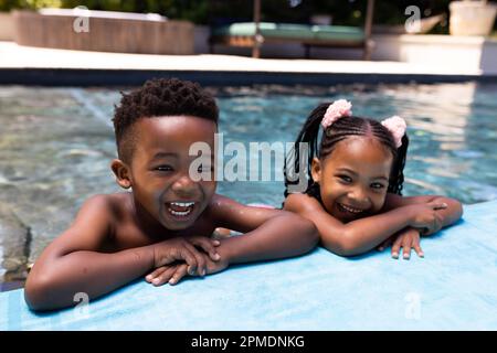 Portrait of cheerful african american siblings laughing while relaxing at poolside in resort Stock Photo