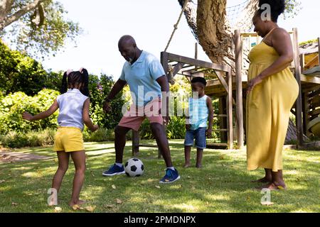African american playful grandparents playing soccer with grandchildren in park Stock Photo