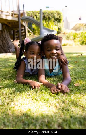 Portrait of cute african american siblings lying on grassy field in park Stock Photo