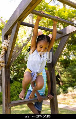 Low angle view of african american girl hanging on monkeys bars at playground Stock Photo