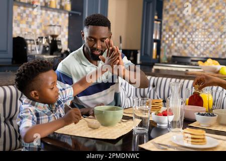 African american father and son giving high-five to each other while having breakfast at home Stock Photo