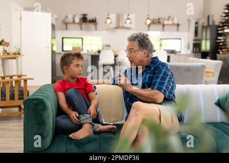Caucasian senior man gesturing and talking with cute grandson while sitting on sofa in living room Stock Photo