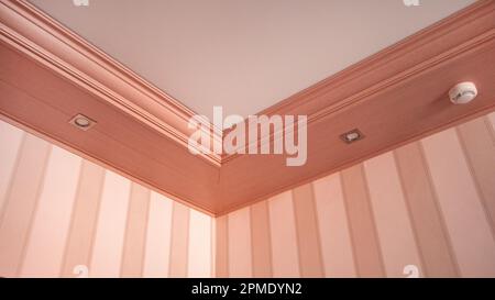 Part of the living room, corner of the wall from the ceiling, mounted LED lights in a wooden console on the ceiling, pink tinting. Stock Photo