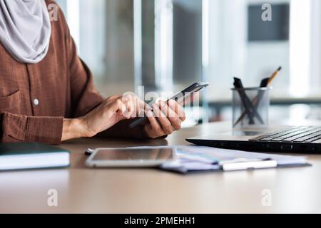 Hands of a female financier use the phone, close-up of a businesswoman at the workplace works with documents inside the office, browses online pages on a smartphone. Stock Photo