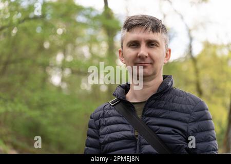 A middle-aged man on a blurred background of early spring greenery looking at camera Stock Photo