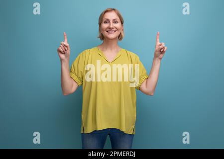 cute blond middle aged woman with an idea points her finger to the side in studio Stock Photo