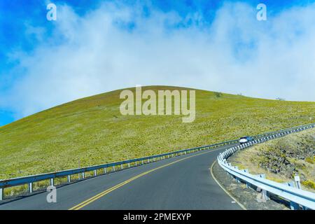 Winding road leading through a single green hill under a blue sky near Mauna Kea. Stock Photo