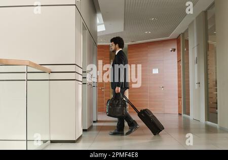 Young businessman in suit with suitcase and bag waiting for elevator standing in office corridor Stock Photo