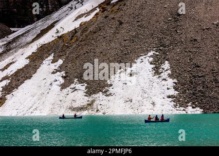 The people are enjoying the tranquil beauty of Moraine lake surrounded by majestic mountains, paddling leisurely in canoes Stock Photo