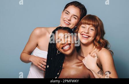 Cheerful women with different skin tones smiling at the camera in a studio. Group of happy young women embracing their natural skin. Portrait of three Stock Photo