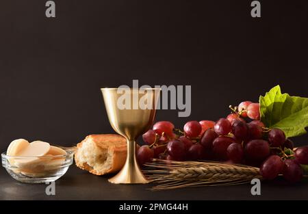 Background of wine glass and wafers with bread and decoration grapes on table and black isolated background. Front view. Stock Photo