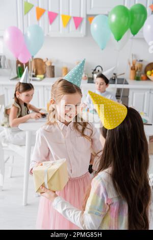 positive birthday girl in party cap receiving present from friend,stock image Stock Photo