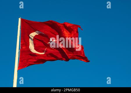 Waving Turkish Flag at sunset isolated on blue sky background. Public holidays of Turkiye. Turk bayragi in Turkish. Stock Photo