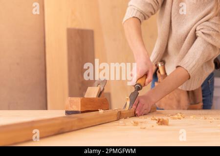 Top view of body part of anonymous carpenter carving wood on plank with chisel on workbench near jack plane while working with lumber in workroom Stock Photo