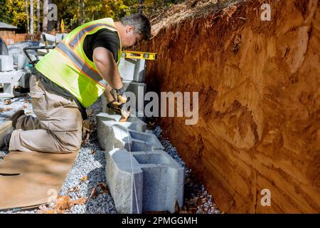 Contractor is constructing block retaining wall on construction site while installing newly constructed wall Stock Photo
