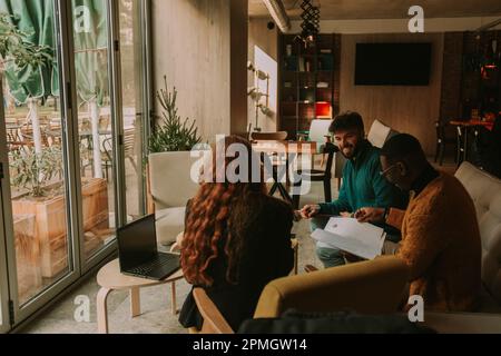Three overjoyed multiracial business people working together on a new project and having fun conversation Stock Photo