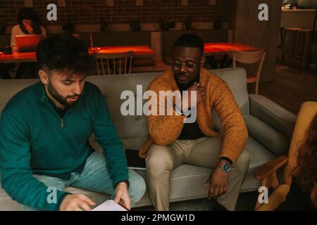Stylish male multiracial colleagues working together remotely at the coffee bar Stock Photo