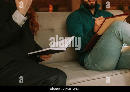 Cooperation between two young business people, male and female. They are sitting on a sofa and discussing financial problems Stock Photo