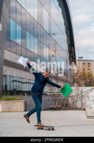 Full length of an attractive smiling young businessman wearing suit, carrying folder while riding skateboard Stock Photo