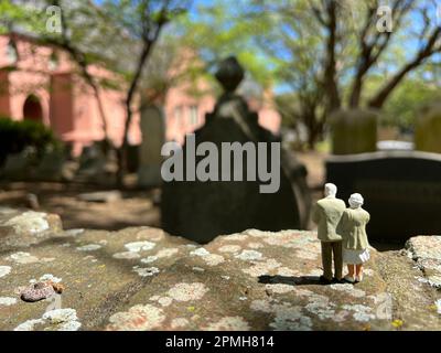 Concept of loss. Miniature people models depict a  white haired senior couple standing together in a cemetery. Stock Photo