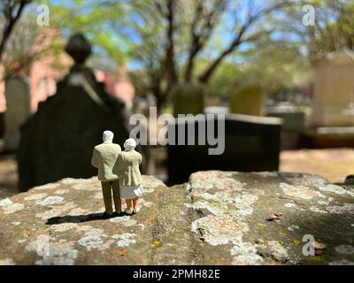 Concept of loss. Miniature people models depict a  white haired senior couple standing together in a cemetery. Stock Photo