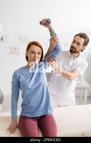 physiotherapist supporting arm of woman training with dumbbell in rehabilitation center,stock image Stock Photo