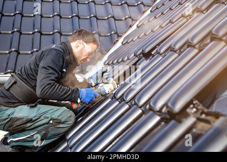 Craftsman using an angle grinder to cut a tile on a roof Stock Photo