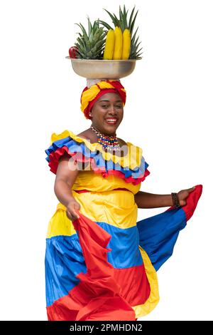 Happy fresh fruit street vendor, Palenquera, dancing on white background. Cheerful Afro-Colombian woman in traditional costumes, Cartagena, Colombia. Stock Photo