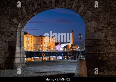 The Albert Dock and Pumphouse viewed through a remnant of the original dock wall at night, Liverpool Waterfront, Liverpool, Merseyside, England Stock Photo
