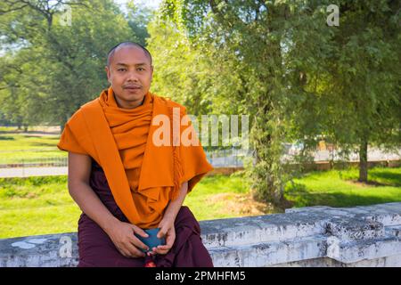 Monk in saffron robe sitting on wall with his cell phone in hand, Royal ...