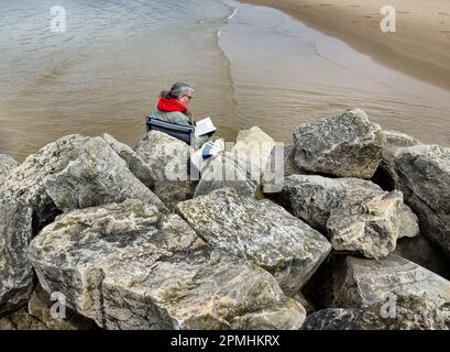 Woman reading a book on beach rock Stock Photo