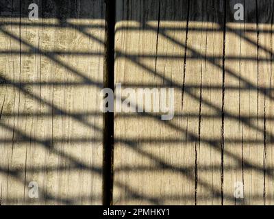 Close-up of lattice fence shadow pattern on brown weathered wood Stock Photo
