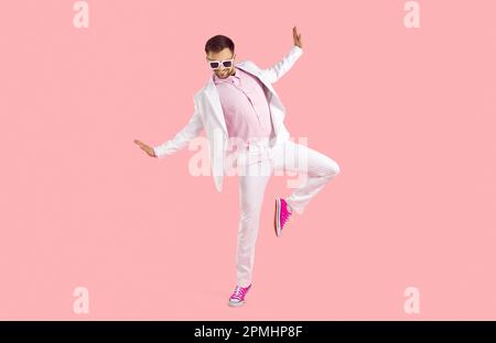 Funny young man in white suit, glasses and trainers dancing isolated on pink background Stock Photo