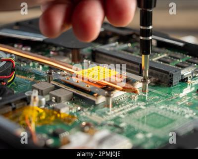 The master repairs a broken laptop with a screwdriver. Specialist and old broken laptop. Stock Photo