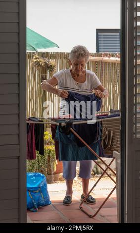 Langebaan, South Africa. 2023. White elderly woman sorting the washing and putting out to dry on a patio. Stock Photo