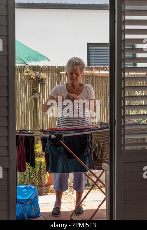 Langebaan, South Africa. 2023. White elderly woman sorting the washing and putting out to dry on a patio. Stock Photo