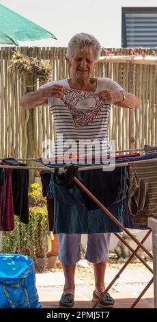 Langebaan, South Africa. 2023. White elderly woman sorting the washing and putting out to dry on a patio. Stock Photo