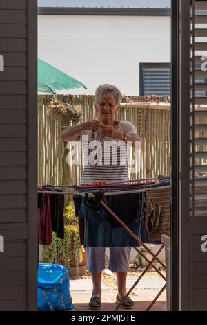 Langebaan, South Africa. 2023. White elderly woman sorting the washing and putting out to dry on a patio. Stock Photo